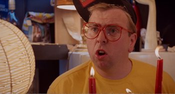 Movie still from “Life Is Sweet” (1990), directed by Mike Leigh – A man wearing a hat and glasses blowing out a birthday candle; Close Up shot, Over the shoulder angle