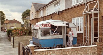 Movie still from “Life Is Sweet” (1990), directed by Mike Leigh – An old food truck parked in front of a brick building; Wide shot, High angle