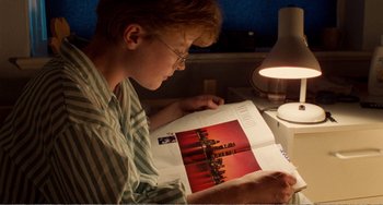 Movie still from “Life Is Sweet” (1990), directed by Mike Leigh – A person sitting at a desk looking at a book; Medium shot, High angle