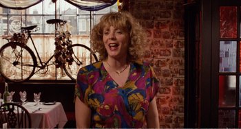 Movie still from “Life Is Sweet” (1990), directed by Mike Leigh – A woman with blonde curly hair wearing a multicolored shirt; Medium shot, Low angle