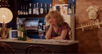 Movie still from “Life Is Sweet” (1990), directed by Mike Leigh – A woman sitting at a table with a glass of wine; Medium shot, High angle