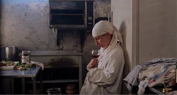 Movie still from “Life Is Sweet” (1990), directed by Mike Leigh – A woman in a kitchen holding a glass of wine; Medium shot, High angle
