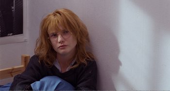 Movie still from “Life Is Sweet” (1990), directed by Mike Leigh – A woman sitting against a wall wearing glasses; Close Up shot, Over the shoulder angle