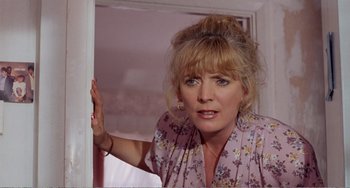 Movie still from “Life Is Sweet” (1990), directed by Mike Leigh – A woman standing in a room with her hand up to her face; Close Up shot, Over the shoulder angle