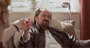 Movie still from “Life Is Sweet” (1990), directed by Mike Leigh – A man sitting on a couch with a cigarette in his hand; Medium shot, Low angle