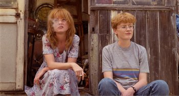 Movie still from “Life Is Sweet” (1990), directed by Mike Leigh – A woman sitting next to a man with a cigarette in her mouth; Medium shot, Low angle