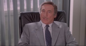 Movie still from “Life Stinks” (1991), directed by Mel Brooks – A man in a suit and tie sitting in a chair; Medium shot, High angle