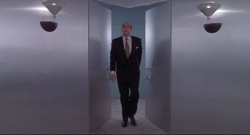 Movie still from “Life Stinks” (1991), directed by Mel Brooks – A man in a suit and tie standing in a doorway; Wide shot, Low angle
