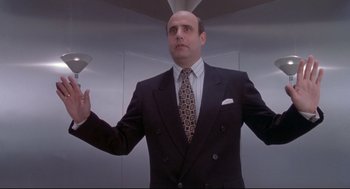 Movie still from “Life Stinks” (1991), directed by Mel Brooks – A man in a suit and tie holding an object in front of him; Medium shot, Low angle