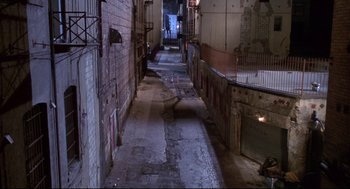 Movie still from “Life Stinks” (1991), directed by Mel Brooks – An alley way with a brick wall and a metal railing on one side; Extreme Wide shot, High angle