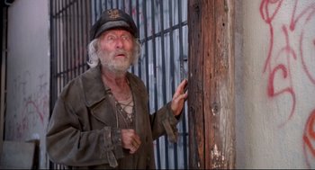 Movie still from “Life Stinks” (1991), directed by Mel Brooks – An old man wearing a hat standing next to a fence; Medium shot, Low angle