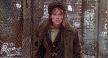 Movie still from “Life Stinks” (1991), directed by Mel Brooks – A woman wearing a hat standing in front of a brick wall; Medium shot, Low angle
