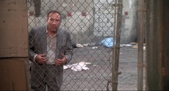 Movie still from “Life Stinks” (1991), directed by Mel Brooks – A man in a suit standing in front of a chain link fence; Medium shot, Low angle