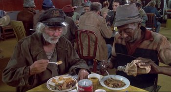 Movie still from “Life Stinks” (1991), directed by Mel Brooks – A group of people sitting at a table with plates of food; Medium shot, High angle