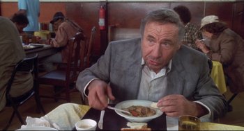 Movie still from “Life Stinks” (1991), directed by Mel Brooks – An older man sitting at a table with a plate of food; Medium shot, High angle