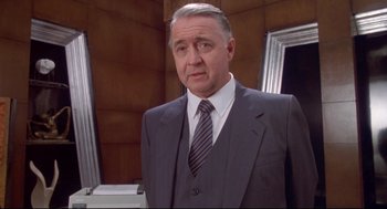 Movie still from “Life Stinks” (1991), directed by Mel Brooks – A man in a suit and tie standing in front of a mirror; Medium shot, Low angle