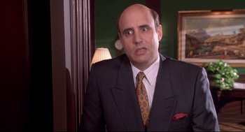Movie still from “Life Stinks” (1991), directed by Mel Brooks – A bald man in a suit and tie in front of a lamp; Close Up shot, Over the shoulder angle