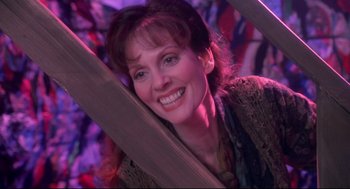 Movie still from “Life Stinks” (1991), directed by Mel Brooks – A woman smiling while holding a wooden structure; Medium shot, Low angle