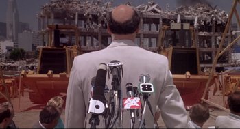 Movie still from “Life Stinks” (1991), directed by Mel Brooks – A man in a white suit is holding microphones; Medium shot, Over the shoulder angle