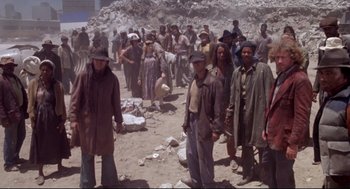 Movie still from “Life Stinks” (1991), directed by Mel Brooks – A group of people standing in the dirt near a pile of rocks; Wide shot, High angle