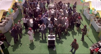 Movie still from “Life Stinks” (1991), directed by Mel Brooks – An overhead view of a crowd of people standing around a table; Extreme Wide shot, High angle