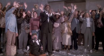 Movie still from “Life Stinks” (1991), directed by Mel Brooks – A group of people standing in front of each other with their hands in the air; Wide shot, Low angle