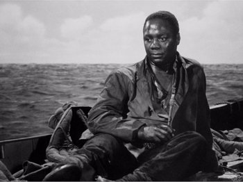 Movie still from “Lifeboat” (1944), directed by Alfred Hitchcock – A black and white photo of a man sitting on a boat; Medium shot, High angle