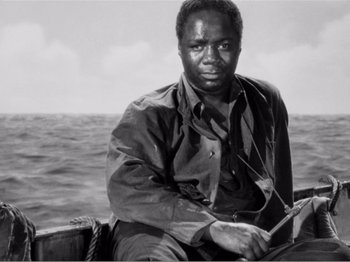 Movie still from “Lifeboat” (1944), directed by Alfred Hitchcock – A black and white photo of a man sitting on a boat; Medium shot, Low angle