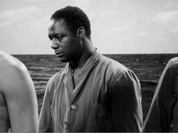 Movie still from “Lifeboat” (1944), directed by Alfred Hitchcock – A black and white photo of a man standing in front of a body of water; Close Up shot, Over the shoulder angle