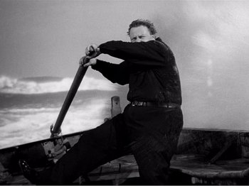 Movie still from “Lifeboat” (1944), directed by Alfred Hitchcock – A black and white photo of a man holding a baseball bat; Medium shot, Low angle