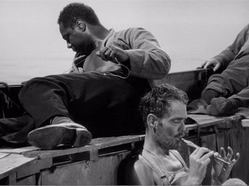 Movie still from “Lifeboat” (1944), directed by Alfred Hitchcock – Two men sitting on a bench and one is shaving his beard; Medium shot, High angle