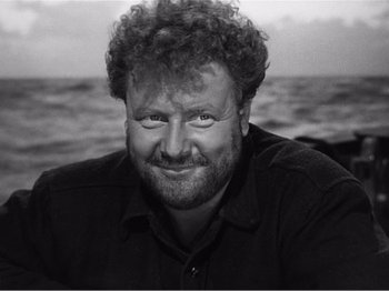 Movie still from “Lifeboat” (1944), directed by Alfred Hitchcock – Black and white photograph of a man smiling at the camera; Close Up shot, High angle
