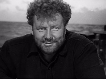 Movie still from “Lifeboat” (1944), directed by Alfred Hitchcock – Black and white photograph of a man smiling for the camera; Close Up shot, High angle
