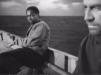 Movie still from “Lifeboat” (1944), directed by Alfred Hitchcock – A man sitting on the side of a boat in front of the ocean; Medium shot, Over the shoulder angle