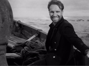 Movie still from “Lifeboat” (1944), directed by Alfred Hitchcock – A black and white photo of a man sitting on a boat; Medium shot, Low angle