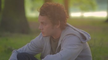 Movie still from “Like Crazy” (2011), directed by Drake Doremus – A man sitting on the ground in the grass; Close Up shot, Over the shoulder angle