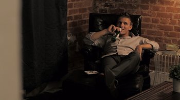 Movie still from “Like Crazy” (2011), directed by Drake Doremus – A man sitting in a chair holding a bottle of beer; Medium shot, Low angle