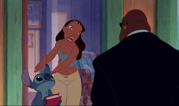 Movie still from “Lilo & Stitch” (2002), directed by Dean DeBlois – A woman holding onto a blue dog while a man watches; Medium shot, Over the shoulder angle