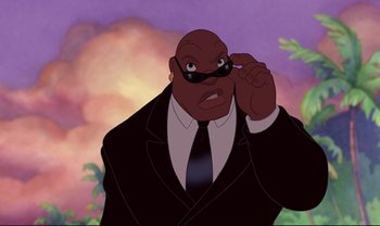 Movie still from “Lilo & Stitch” (2002), directed by Dean DeBlois – A man in a suit and tie holding a pair of sunglasses; Close Up shot, Low angle