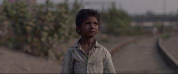 Movie still from “Lion” (2016), directed by Garth Davis – A young boy standing on the side of a road; Close Up shot, Low angle