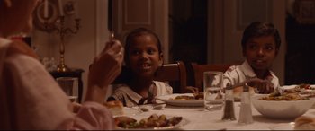 Movie still from “Lion” (2016), directed by Garth Davis – A child sitting at a table with a plate of food; Medium shot, High angle
