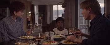 Movie still from “Lion” (2016), directed by Garth Davis – A boy sitting at a table with a plate of food in front of him; Medium shot, Over the shoulder angle