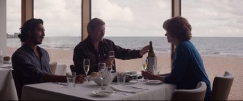 Movie still from “Lion” (2016), directed by Garth Davis – Two people sitting at a table with a bottle of wine; Medium shot, Over the shoulder angle