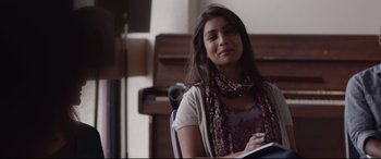 Movie still from “Lion” (2016), directed by Garth Davis – A woman sitting in a chair with a book in her hand; Medium shot, Over the shoulder angle