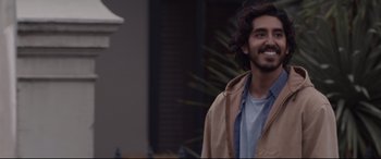 Movie still from “Lion” (2016), directed by Garth Davis – A man with long hair and a beard smiling; Close Up shot, Over the shoulder angle