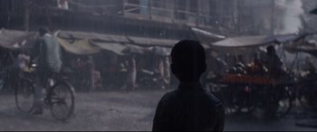 Movie still from “Lion” (2016), directed by Garth Davis – A man standing in the rain looking out of a window; Wide shot, High angle