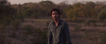 Movie still from “Lion” (2016), directed by Garth Davis – A man standing in the middle of a field with trees in the background; Medium shot, Over the shoulder angle
