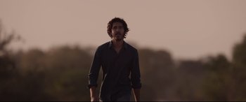 Movie still from “Lion” (2016), directed by Garth Davis – A man in a black shirt is standing in the grass; Medium shot, Low angle