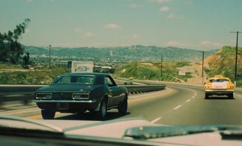 Movie still from “Lions Love (... and Lies)” (1969), directed by Agnès Varda – A car driving down a road with a mountain in the background; Wide shot, High angle