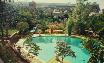 Movie still from “Lions Love (... and Lies)” (1969), directed by Agnès Varda – A woman standing next to a swimming pool in a yard; Extreme Wide shot, High angle